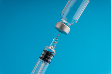 Medical syringe and vial on blue background with selective focus and crop fragment