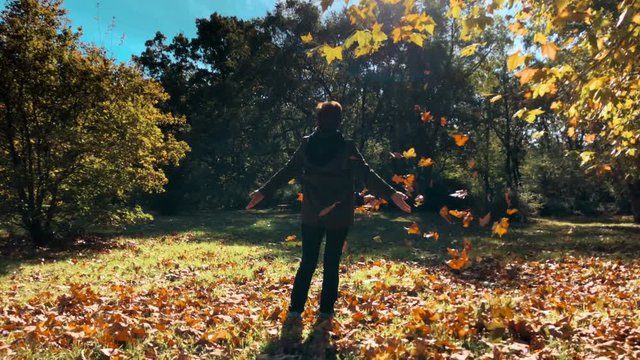 A woman on her back enjoys throwing leaves in the air in a forest in autumn