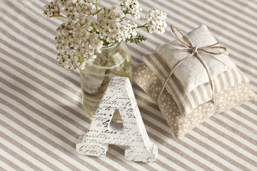 Nostalgic still life with white flowers, letter A and decorative little cushions