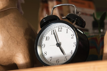 Naklejka premium Black retro alarm clock is on the shelf and shows five o'clock. vintage watch. tea time. early awakening