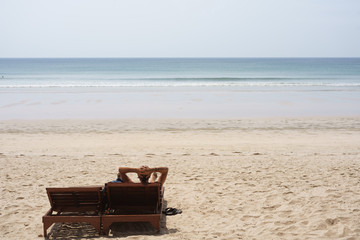 A man is relaxing on a chair on the beach