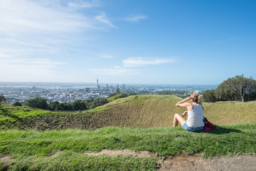 Fototapeta na wymiar Tourist relaxing on Mount Eden crater and looking to Auckland the largest city in North island of New Zealand.