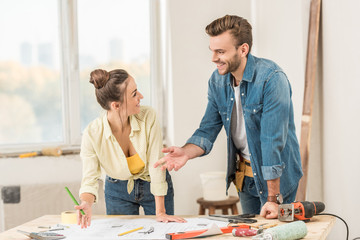 happy young couple discussing blueprint and smiling each other during renovation