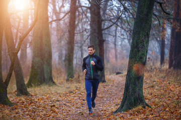 Young man jogging in autumn park in the morning