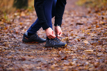 Young man runner lacing up shoelaces on trail