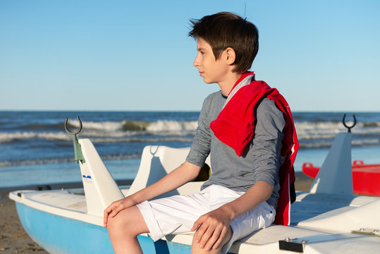Young boy sitting on catamaran at the summer beach. Cute spectacled smiling happy 12 years old boy at seaside. Kid's outdoor portrait over seaside.