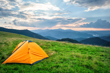 Orange tourist tent in mountains covered with green grass