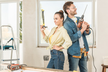 happy young couple holding tools and standing back to back during renovation
