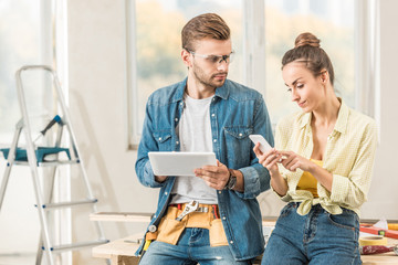 young couple using digital devices during repairment