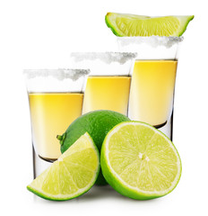 Three glasses of golden tequila with whole and sliced lime stand
