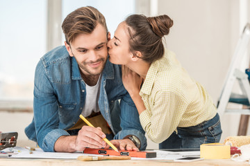 Fototapeta premium young woman kissing smiling man marking blueprint with level tool
