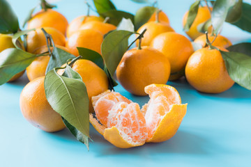 Fresh whole mandarins and slice with leaves on blue table. Healthy eating concept.