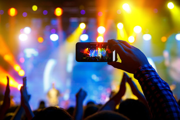 People in the crowd at a concert make video recordings and pics on a smartphone