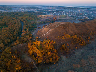 Hill with beautiful autumn trees. Blue fog. Sunrise mood moment. City at the background. Drone aerial photo