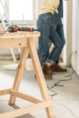 electric drill on wooden table and young couple standing near wall behind