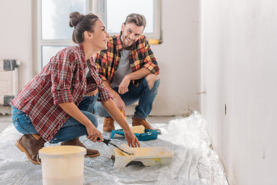 happy young couple in checkered shirts painting wall together in new apartment
