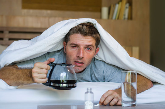 lifestyle home portrait of young exhausted and wasted man waking up suffering headache and hangover after drinking alcohol at night party lying on bed sick
