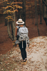 Young woman in a stylish hat and travel bag on her shoulders, looking around at the charming autumn forest