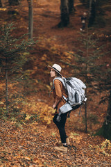 Woman in a stylish hat and travel bag on her shoulders, looking around at the charming autumn forest