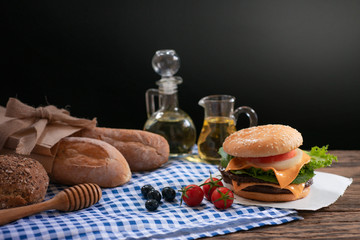 Close up of homemade hamburger with fresh vegetables on paper and oil glasses in background , black background