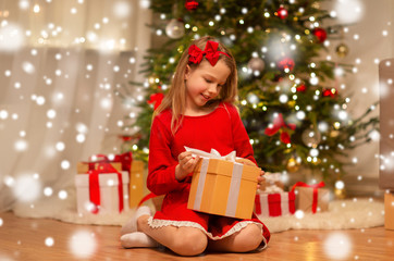christmas, holidays and childhood concept - smiling girl in red dress with gift box at home