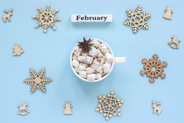 Winter composition. Wooden calendar winter month February Mug of cocoa with marshmallows and anise star surrounded by large wooden snowflakes on blue background. Top view Flat lay Greeting card