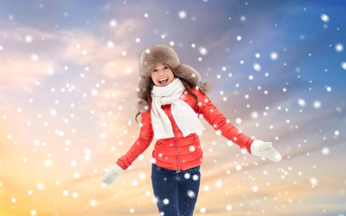 people, season and leisure concept - happy woman in winter fur hat having fun outdoors over sky background and snow