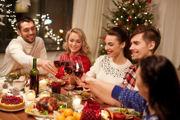 holidays and celebration concept - happy friends having christmas dinner at home, drinking red wine and clinking glasses