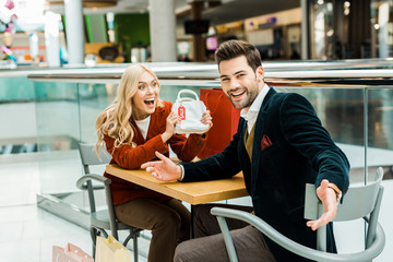 excited female shopaholic showing bag with sale tag to laughing boyfriend
