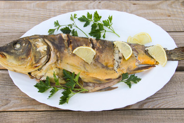Tasty baked carp in white plate on wooden table. Top view