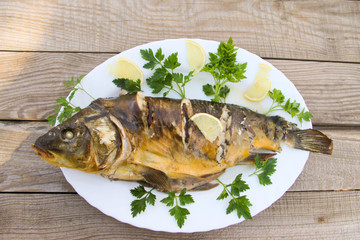 Tasty baked carp in white plate on wooden table. Top view