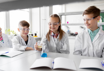 Fototapeta premium education, science, chemistry and children concept - kids or students with test tube making experiment at school laboratory