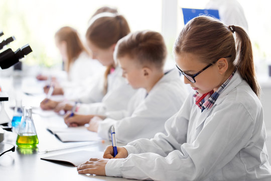 education, science and children concept - teacher and kids studying chemistry at school laboratory and writing to workbooks