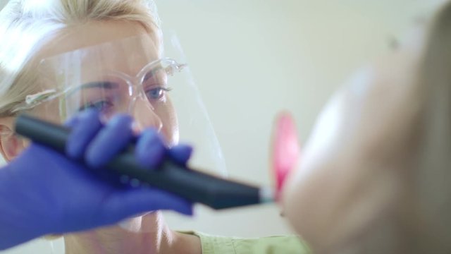 Dentist using dental curing light for oral cavity. Dental composite polymerization procedure. Close up of woman doctor working with patient in dental clinic. Professional teeth filling