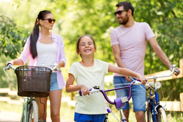 family, leisure and people concept - happy mother, father and little daughter with bicycles in summer park