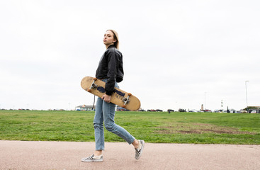 Teenage girl walking in park while holding her skate board