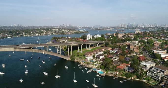 Shores of Drummoyne suburbs along Parramatta river near Gladesville bridge in view of distant Sydney city CBD cityscape.
