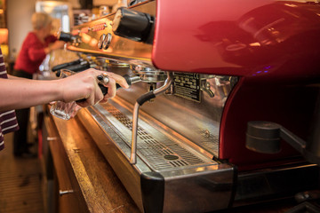 Cropped shot of barista using a coffee maker to prepare a cup of coffee. Female cafe worker making a coffee.