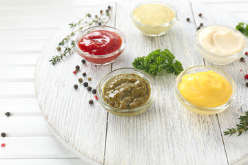 Different tasty sauces in bowls on white wooden board