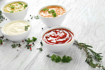 Different tasty sauces in bowls with spices on white wooden table
