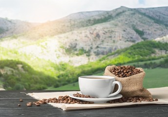 Cup of hot coffee with beans on background