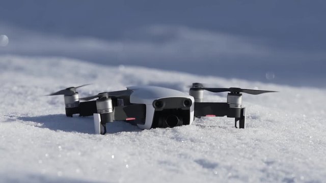 Close-up shot of a small white drone taking off from snow in slow motion