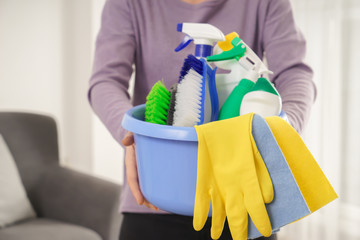 Woman with basin full of cleaning supplies at home, closeup