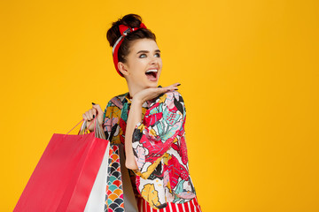 Young happy caucasian woman in casual colorful clothes holding bags and shopping over orange background.