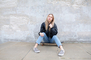 Teenage girl sitting on a skate board posing for a picture