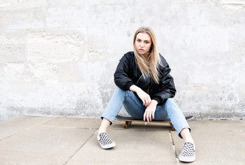 Teenage girl sitting on a skate board posing for a picture