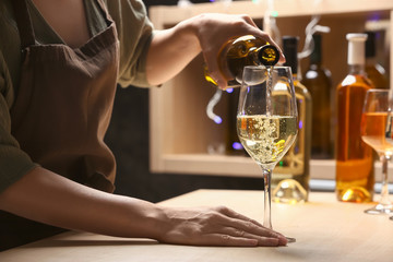 Female barman pouring wine from bottle into glass on counter