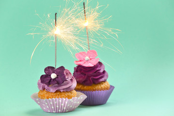 Tasty birthday cupcakes with sparklers on color background