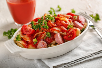 Delicious pasta with sausage and sauce in ceramic dish on light table