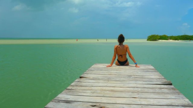 A young girl sitting in a Caribbean pier at Holbox